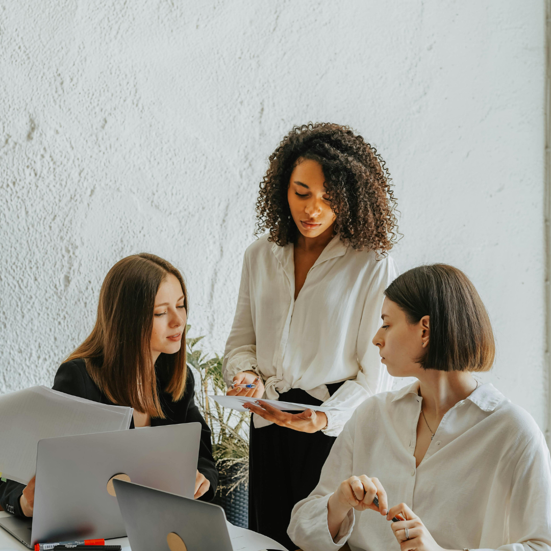 Three professional women in a modern office discussing digital strategy, representing teamwork and collaboration on what competitors are doing online to improve visibility.