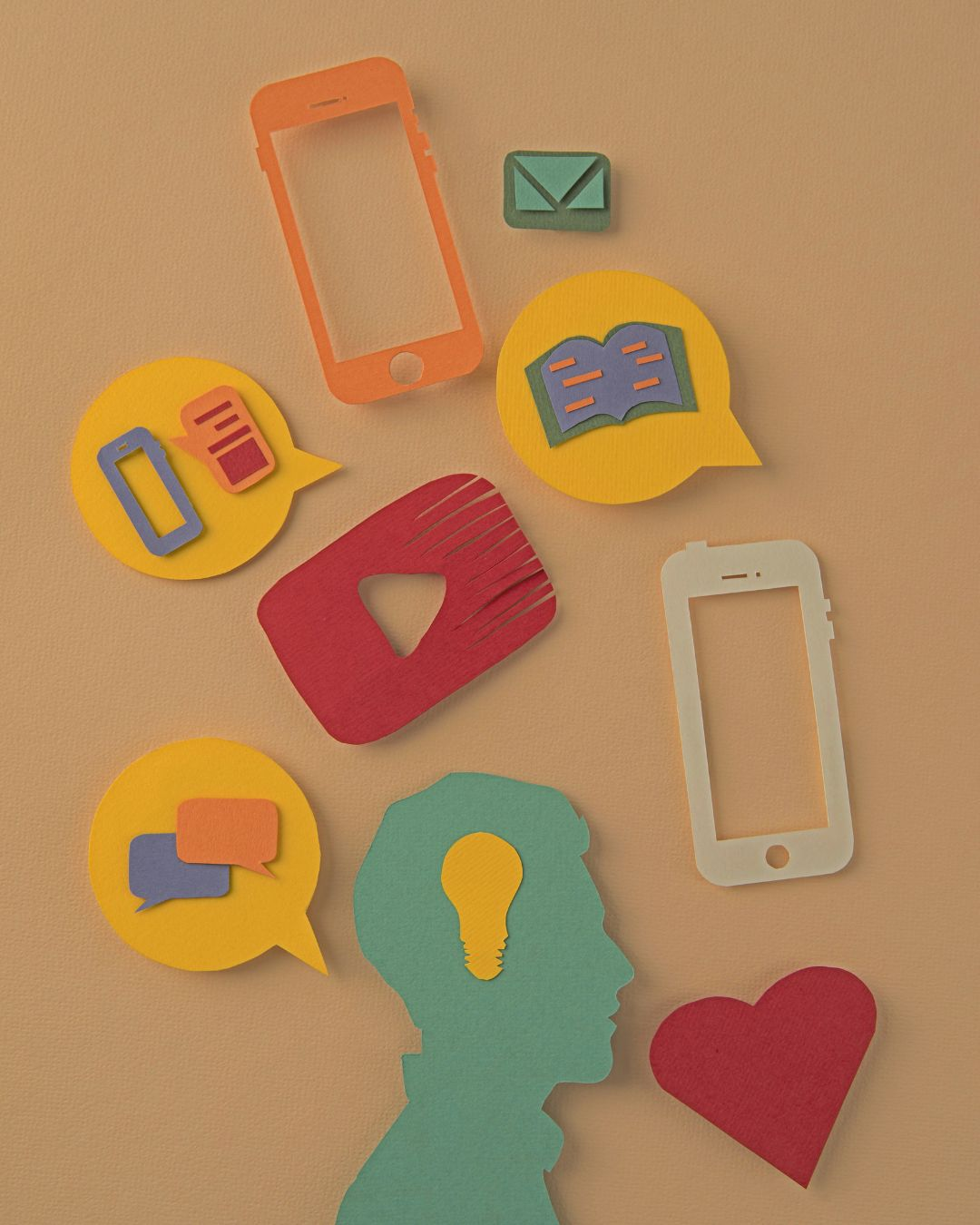 Colorful paper cutouts of phones, speech bubbles, email, a YouTube play button, and a heart surrounding a silhouette with a light-bulb idea