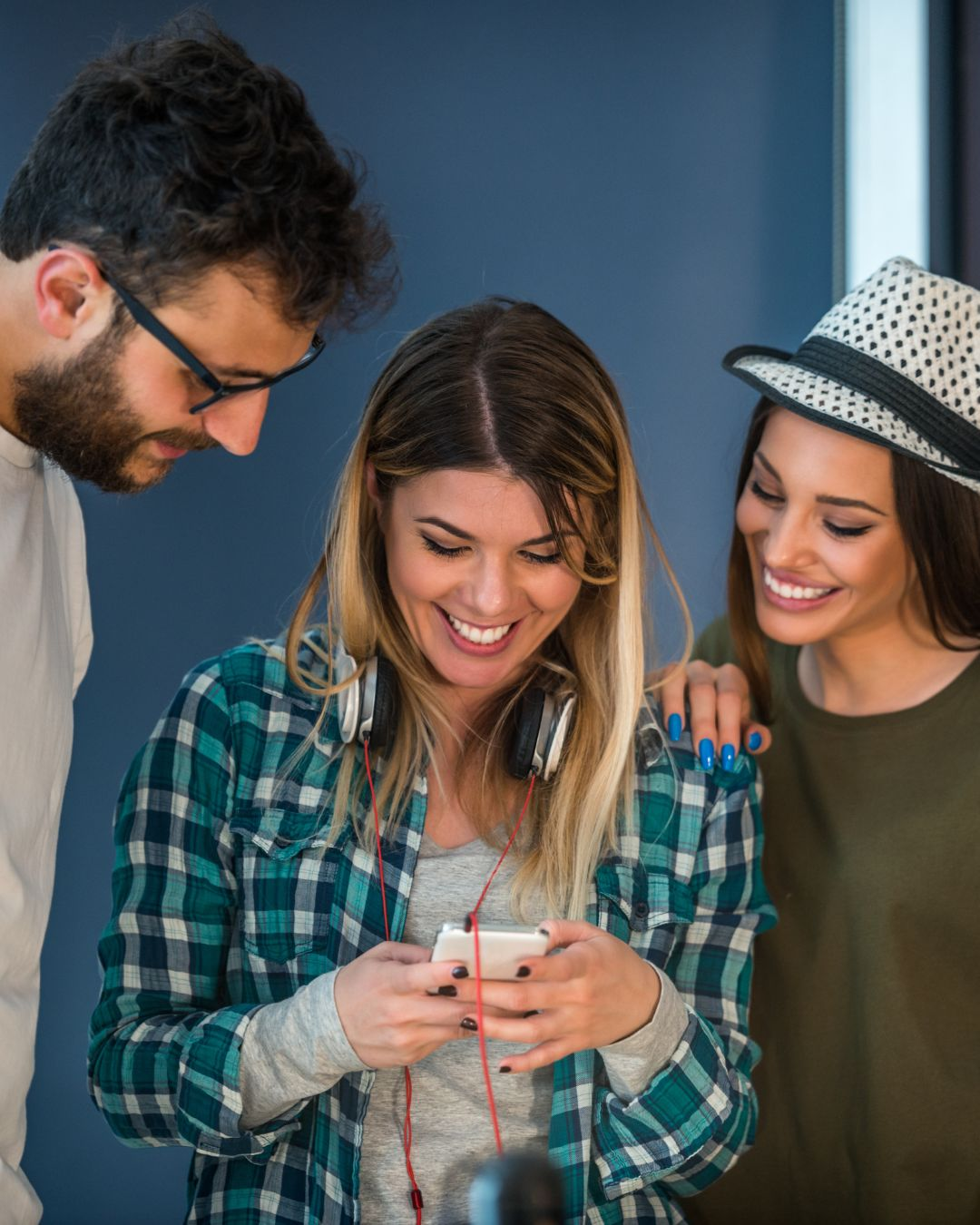 Three young colleagues gathered around a smartphone, smiling as they catch up on social media trends to avoid missed social media trends.