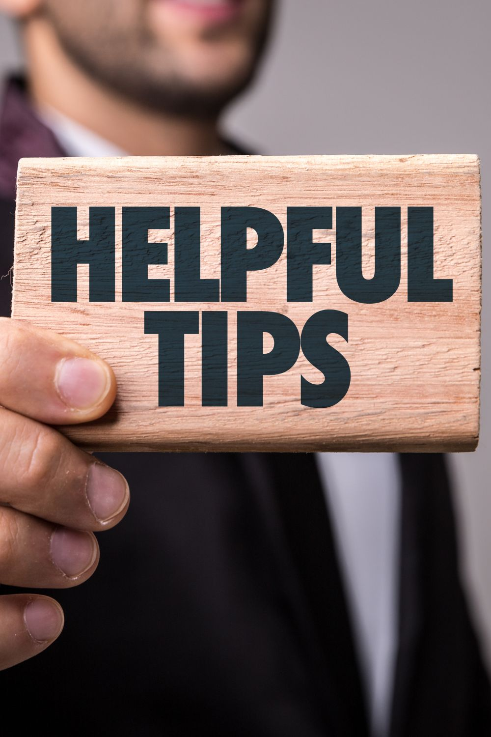 Businessman holding a wooden sign with the words Helpful Tips written in bold letters.