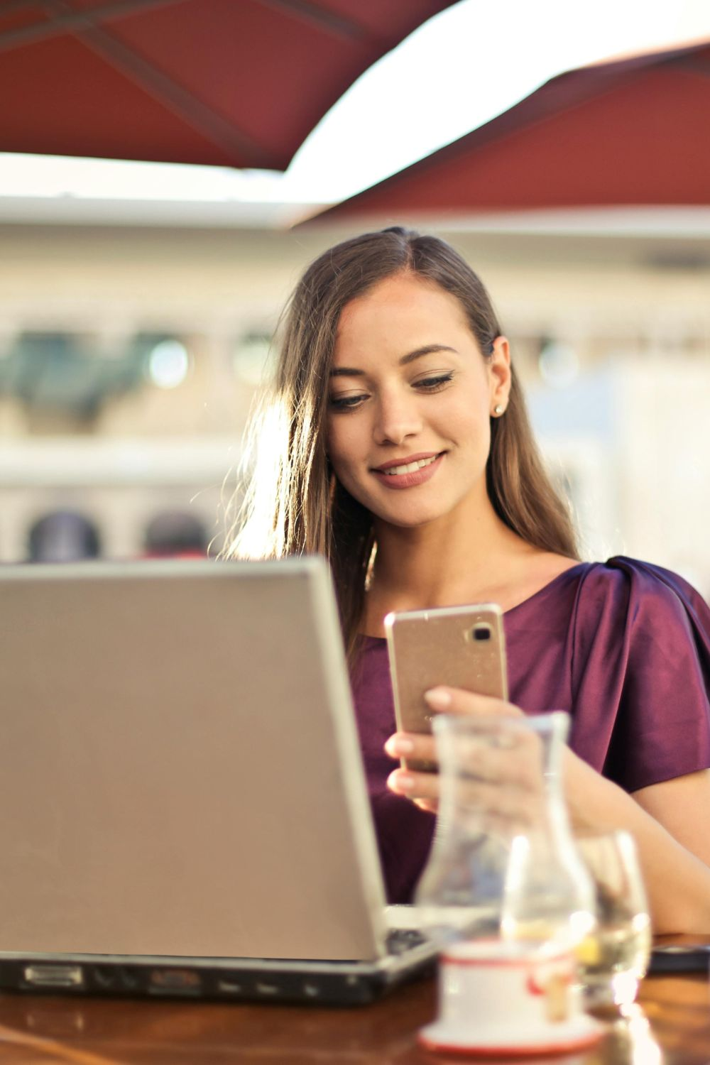 Woman sitting at a café using a smartphone and laptop, representing modern social media campaign strategies in 2025.