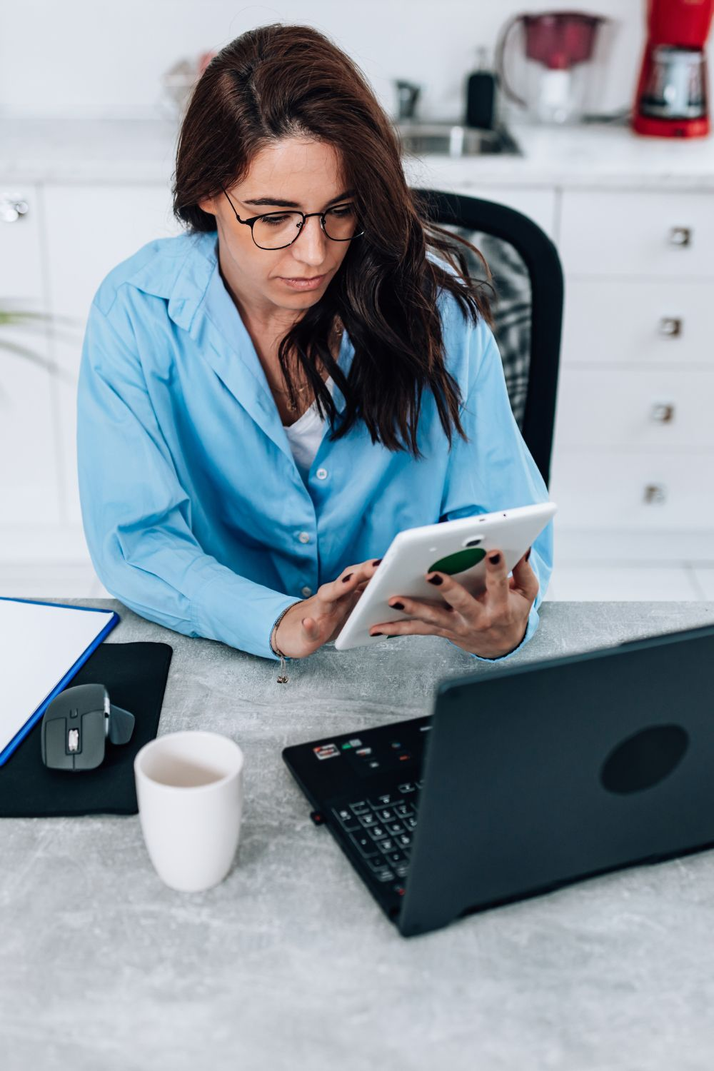 Woman in blue shirt working at a desk with a tablet and laptop, focusing on digital strategy and business planning.