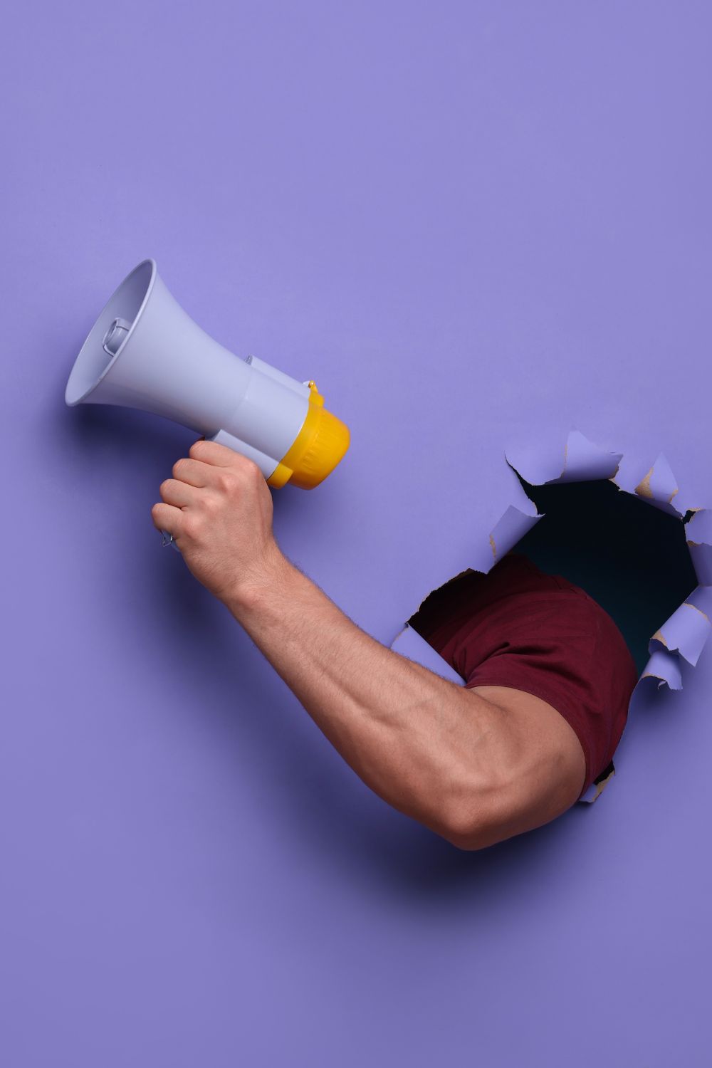 Hand holding a megaphone through torn purple paper, symbolizing social media campaign promotion.
