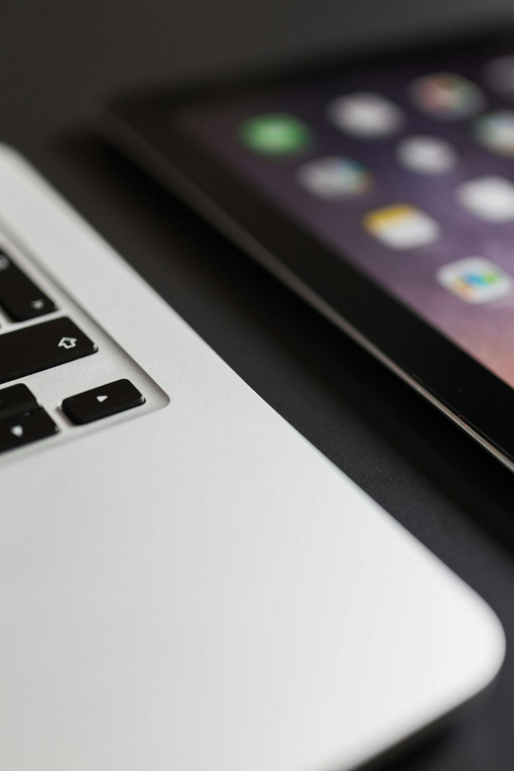 Close-up of a laptop keyboard next to a tablet screen displaying app icons, symbolizing digital tools for social media and online marketing.