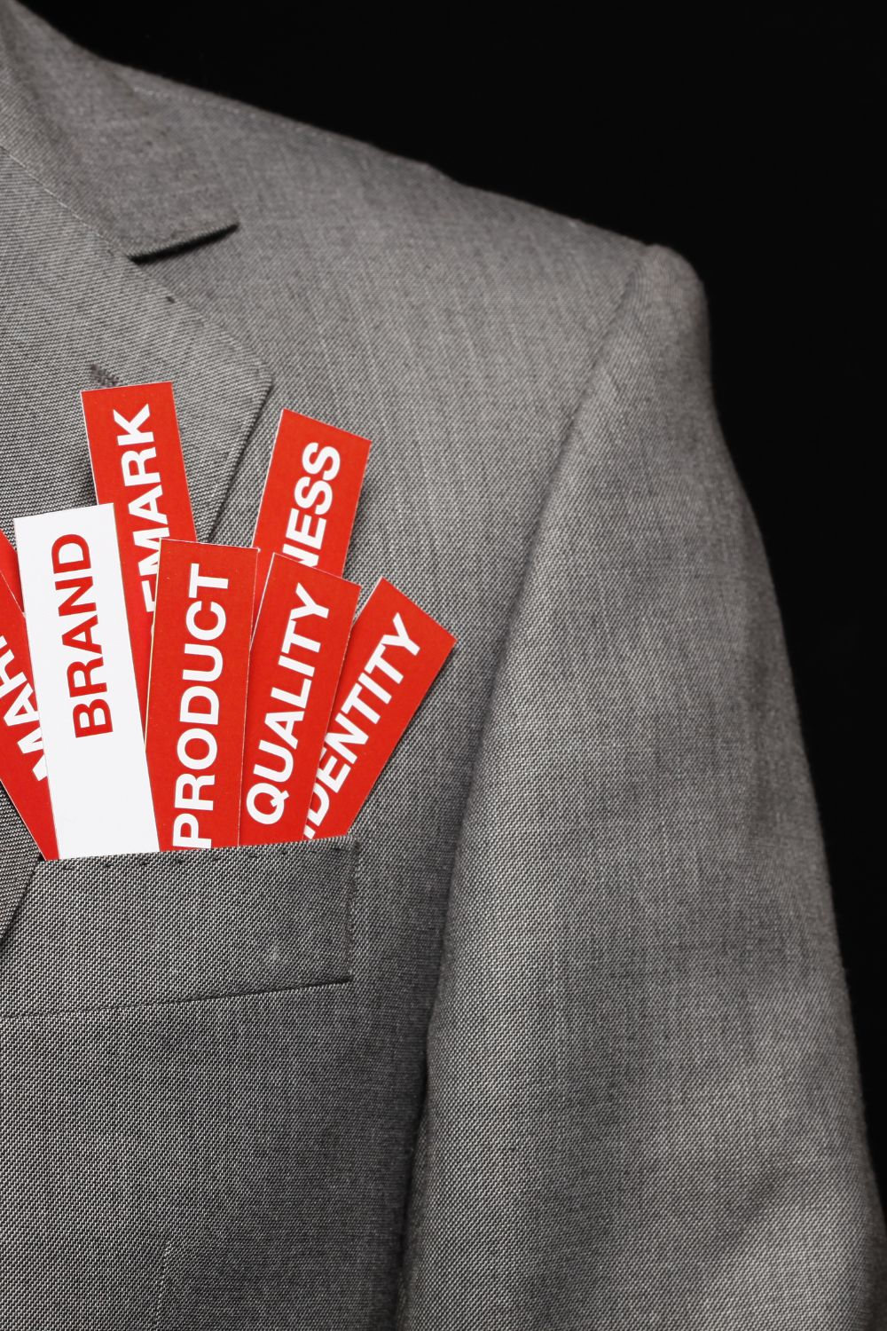 Gray suit pocket filled with red cards labeled Brand, Product, Quality, and Identity, representing business branding elements.